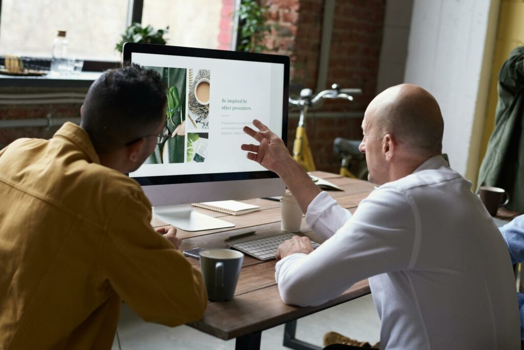Two colleagues collaborating on a project in a modern office setting with a computer display and coffee.