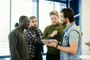 Team of diverse young adults discussing project on digital tablet in modern office environment.