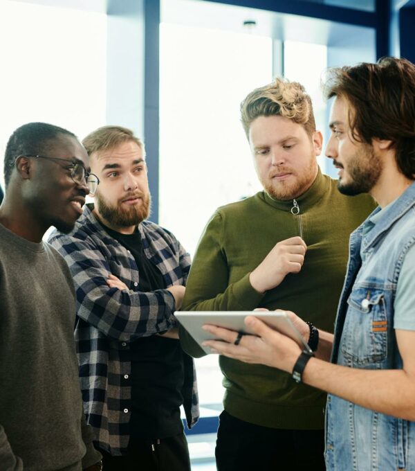 Team of diverse young adults discussing project on digital tablet in modern office environment.