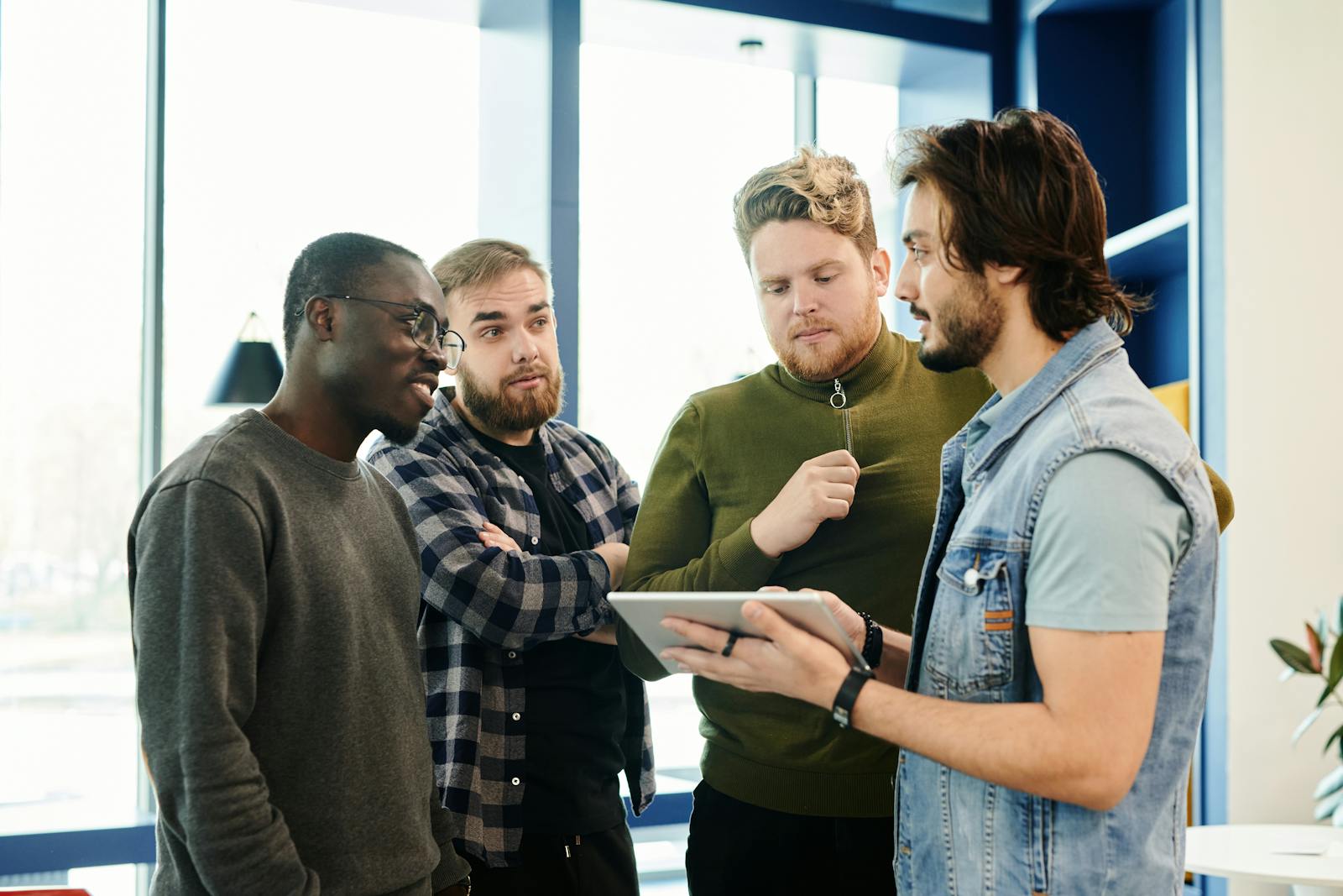 Team of diverse young adults discussing project on digital tablet in modern office environment.